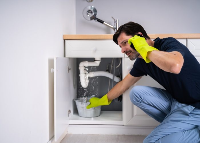 Sad,Young,Man,Calling,Plumber,In,Front,Of,Water,Leaking